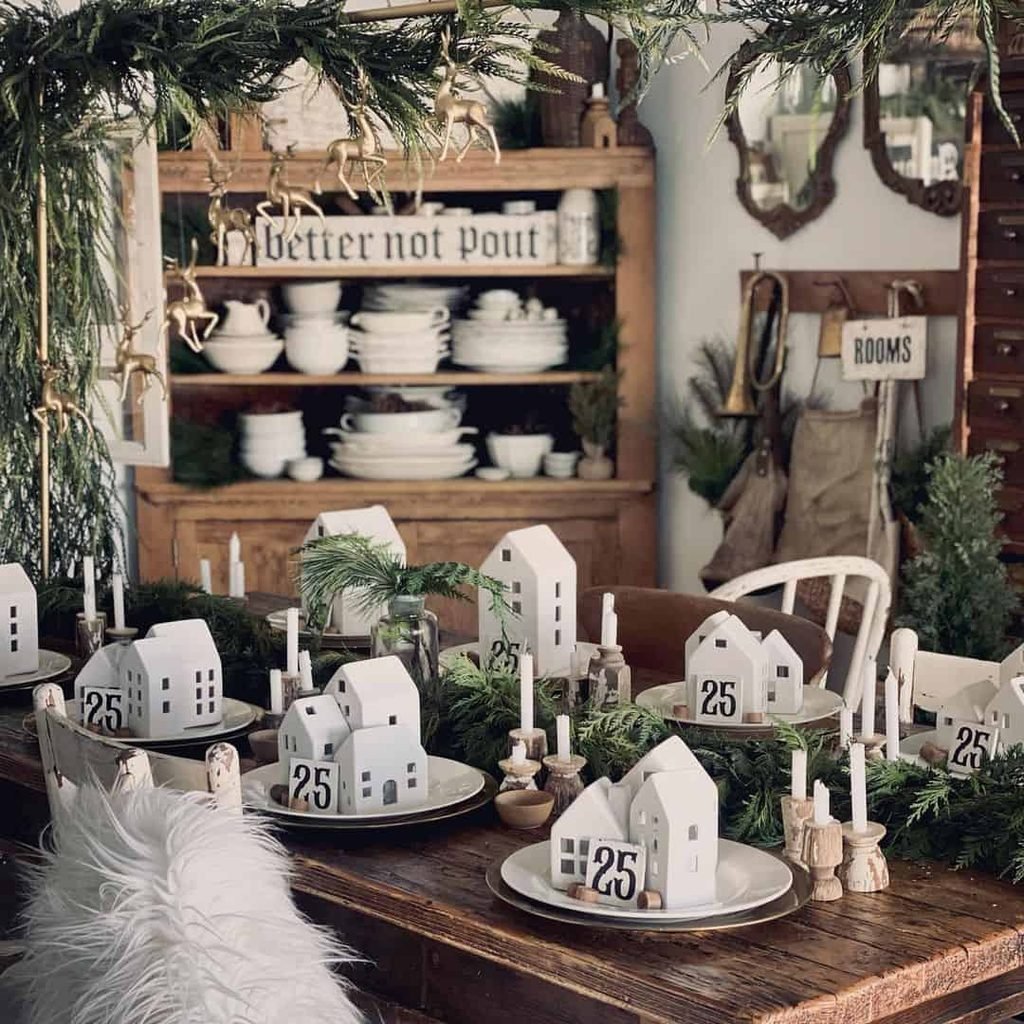 Minimal Christmas table centerpiece with small cream ceramic houses and evergreen branches