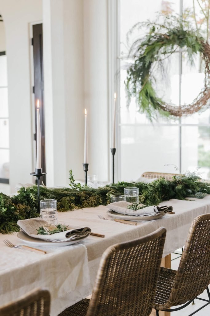 Minimal Christmas dining table with a ceramic vase, evergreen branches, cream linen, and simple tableware