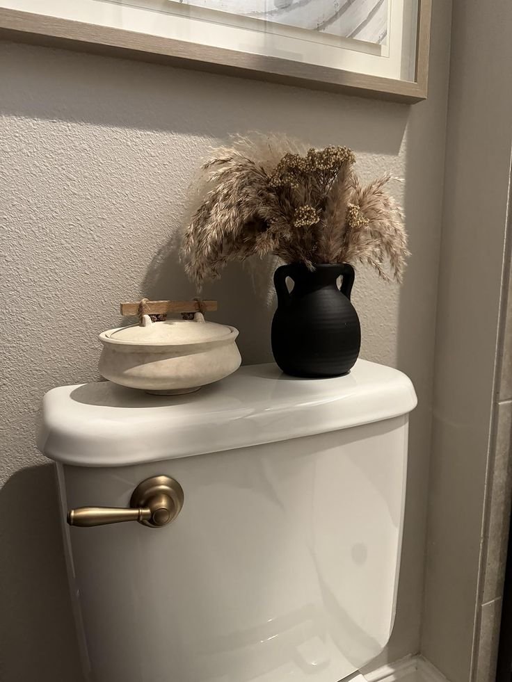 Small ceramic vase decorating the top of a toilet tank