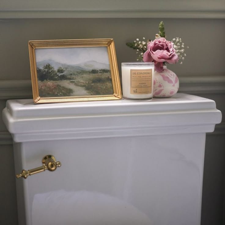 Small framed artwork leaning behind a decorated toilet tank