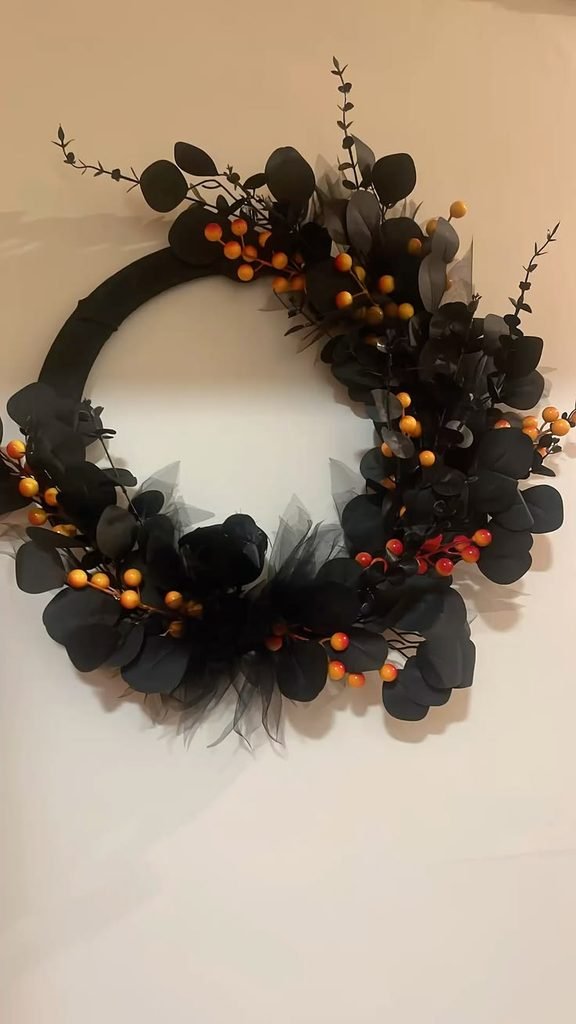 Black Halloween floral wreath with purple foliage and a small raven on a wooden door.
