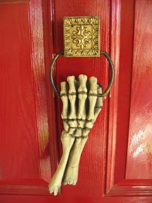 Antique-style skeleton hand door knocker on a burgundy Halloween front door.