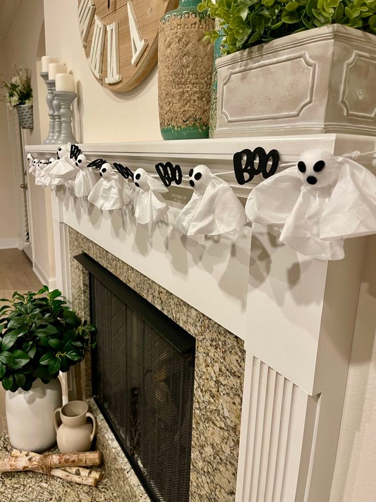 Cute Halloween fireplace mantel with a white ghost garland and ceramic pumpkins.