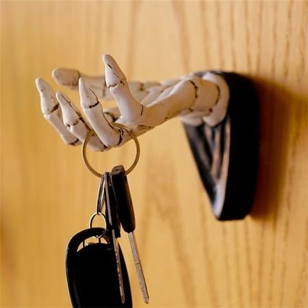Skeleton hand wall hooks holding Halloween accessories above a narrow hallway bench.