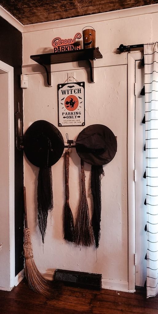 Vintage witch's broom with burgundy ribbon and black pumpkin in a Halloween hallway corner.