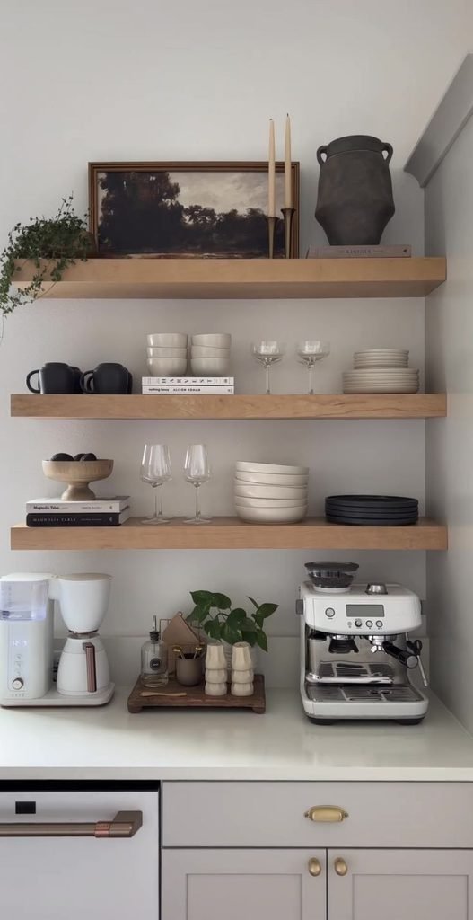 Coffee bar with open wooden shelves displaying ceramic mugs, coffee canisters, glass jars, and a small plant