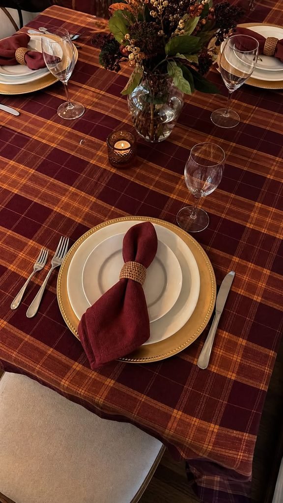 Cozy Thanksgiving table with plaid napkins, neutral stoneware, wood accents, and seasonal greenery.