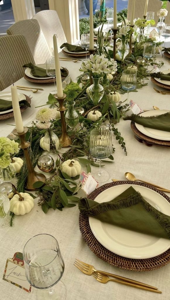Moody green Thanksgiving tablescape with olive linens, cream plates, greenery, and brass accents.