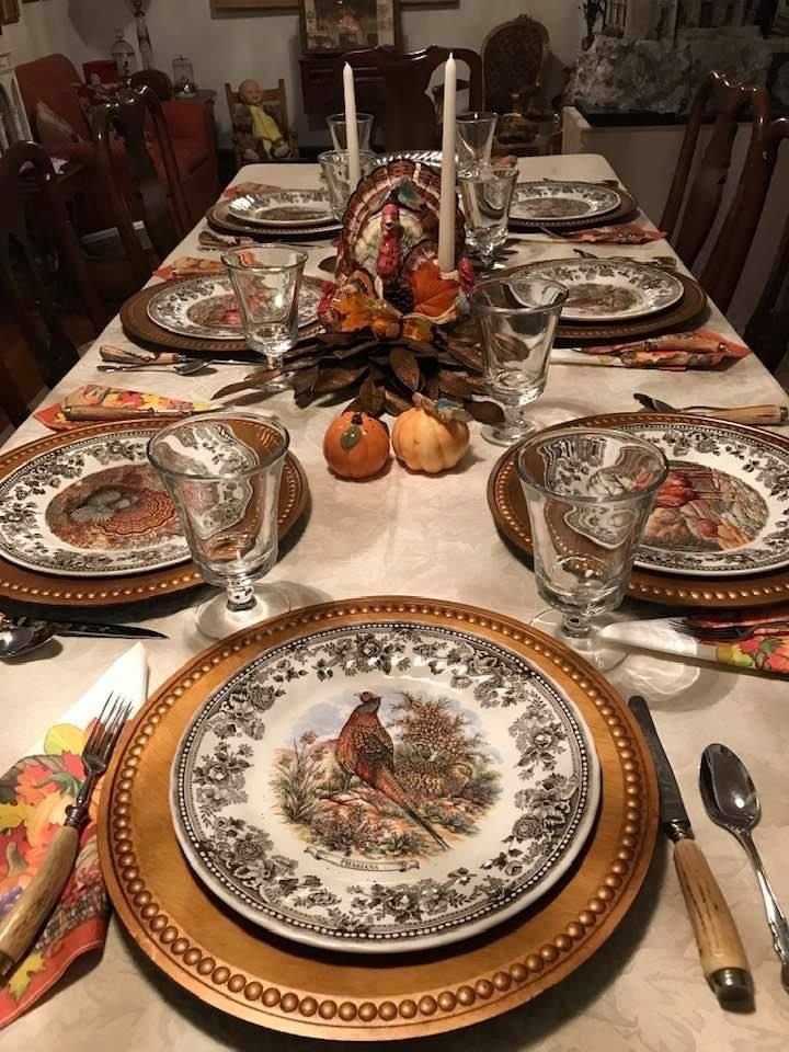 Vintage Thanksgiving table with mismatched floral china, glassware, linen napkins, and greenery.