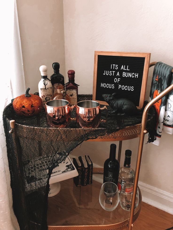 Halloween drink station with glass dispensers, colorful party drinks, vintage glasses, and spooky decorations.