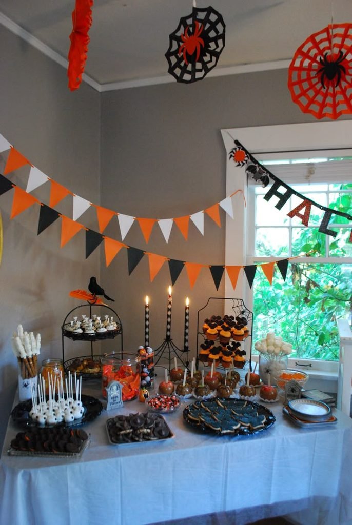 Halloween dessert display with cupcakes, ghost cookies, caramel apples, and seasonal decorations.