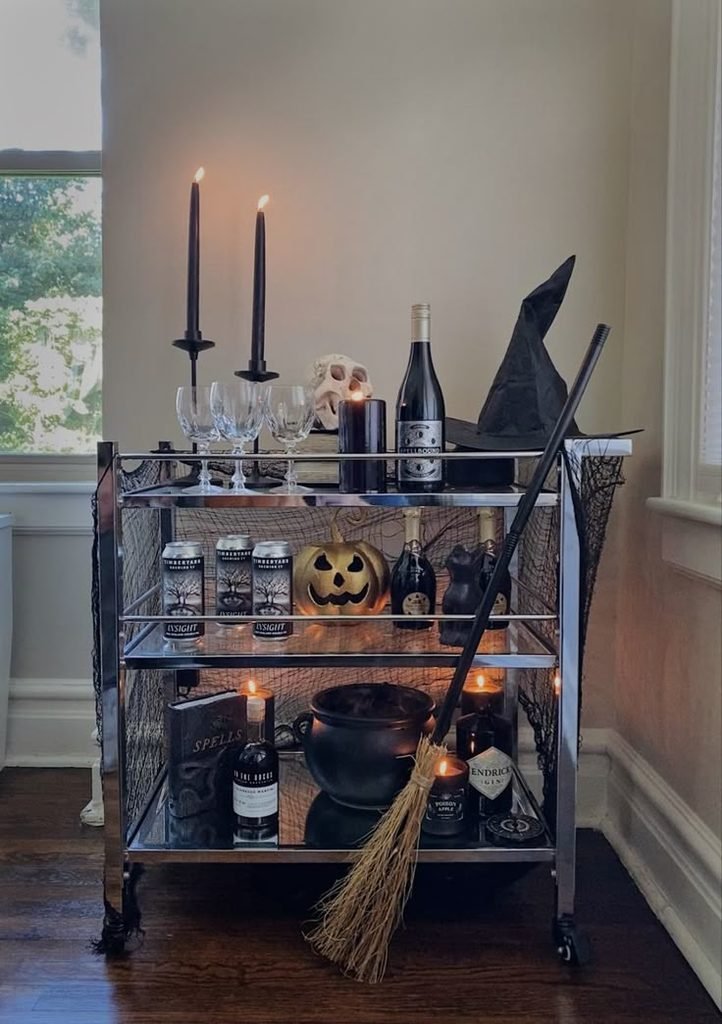 Halloween bar cart with vintage glasses, a red drink pitcher, amber bottles, and dark floral decor.