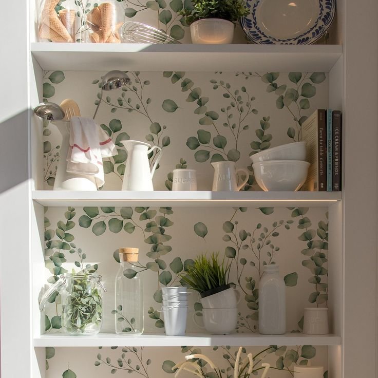 Open wood shelves with botanical leaf wallpaper, ceramic decor, books, and a small plant