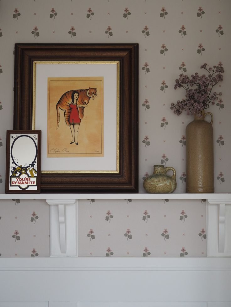 Small floral wallpaper behind narrow shelf wallpaper with neutral ceramic decor and books
