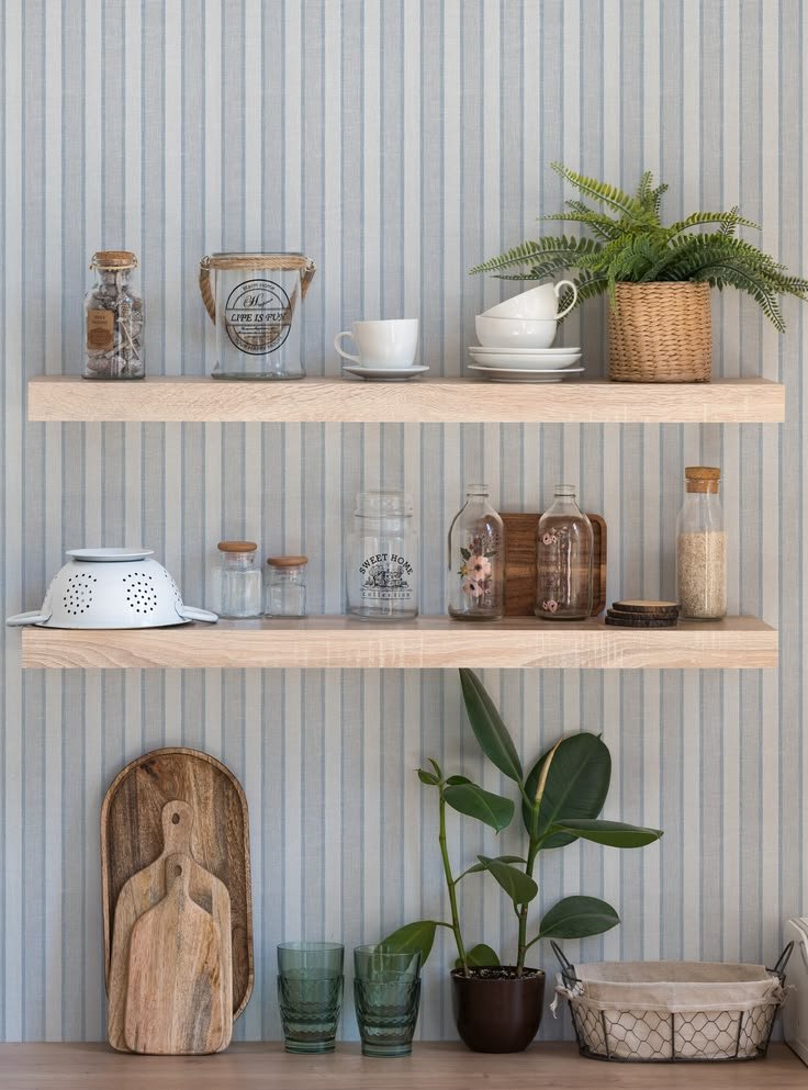 Striped wallpaper behind light wood shelves styled with books, ceramics, and decorative objects
