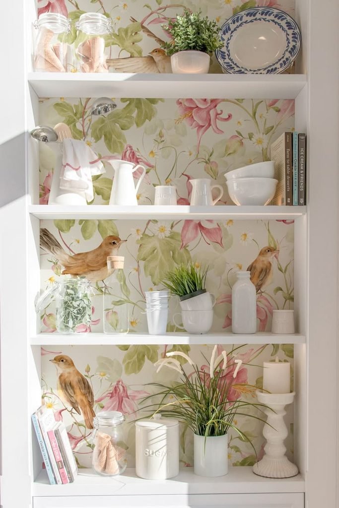 Bird and nature wallpaper behind shelves styled with ceramic vases, books, and wood decor