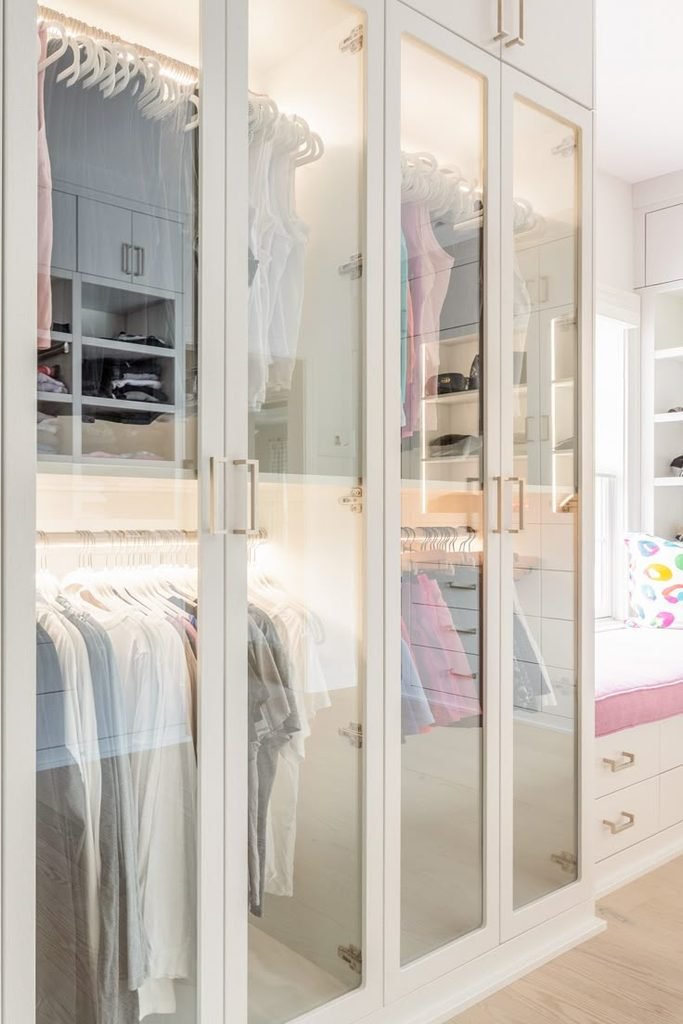 Elegant closet with fluted glass wardrobe doors, warm lighting, and neatly arranged clothing.