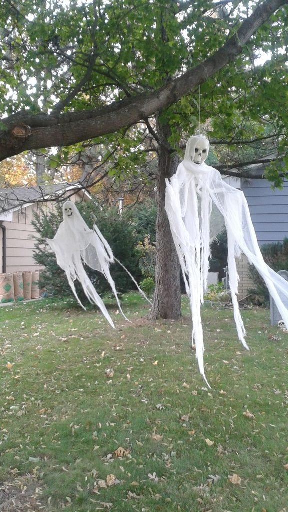 White hanging ghost decorations suspended from trees in a Halloween garden.