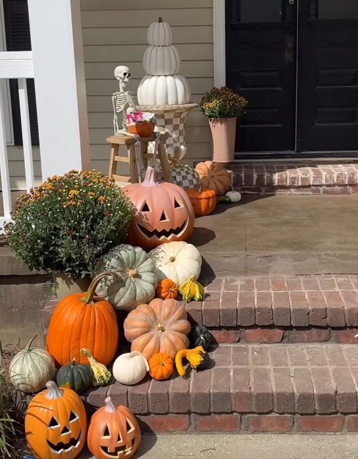 Orange, cream, and green pumpkins stacked beside outdoor front steps.