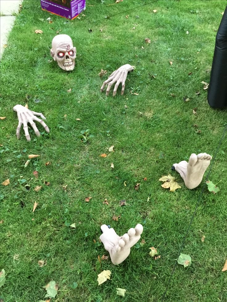 Fake skeletal hands emerging from a leaf-covered garden bed for Halloween.