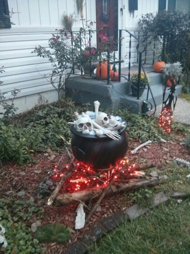 Outdoor Halloween witch's cauldron surrounded by potion bottles and pumpkins.