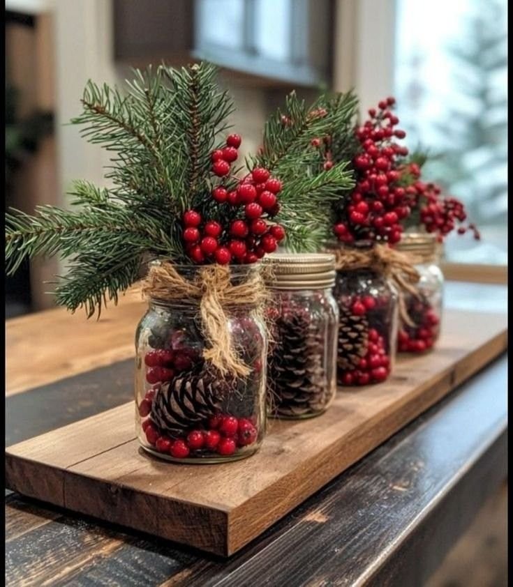 Christmas mason jar centerpiece with evergreen branches, red berries, pinecones, and red ribbon.